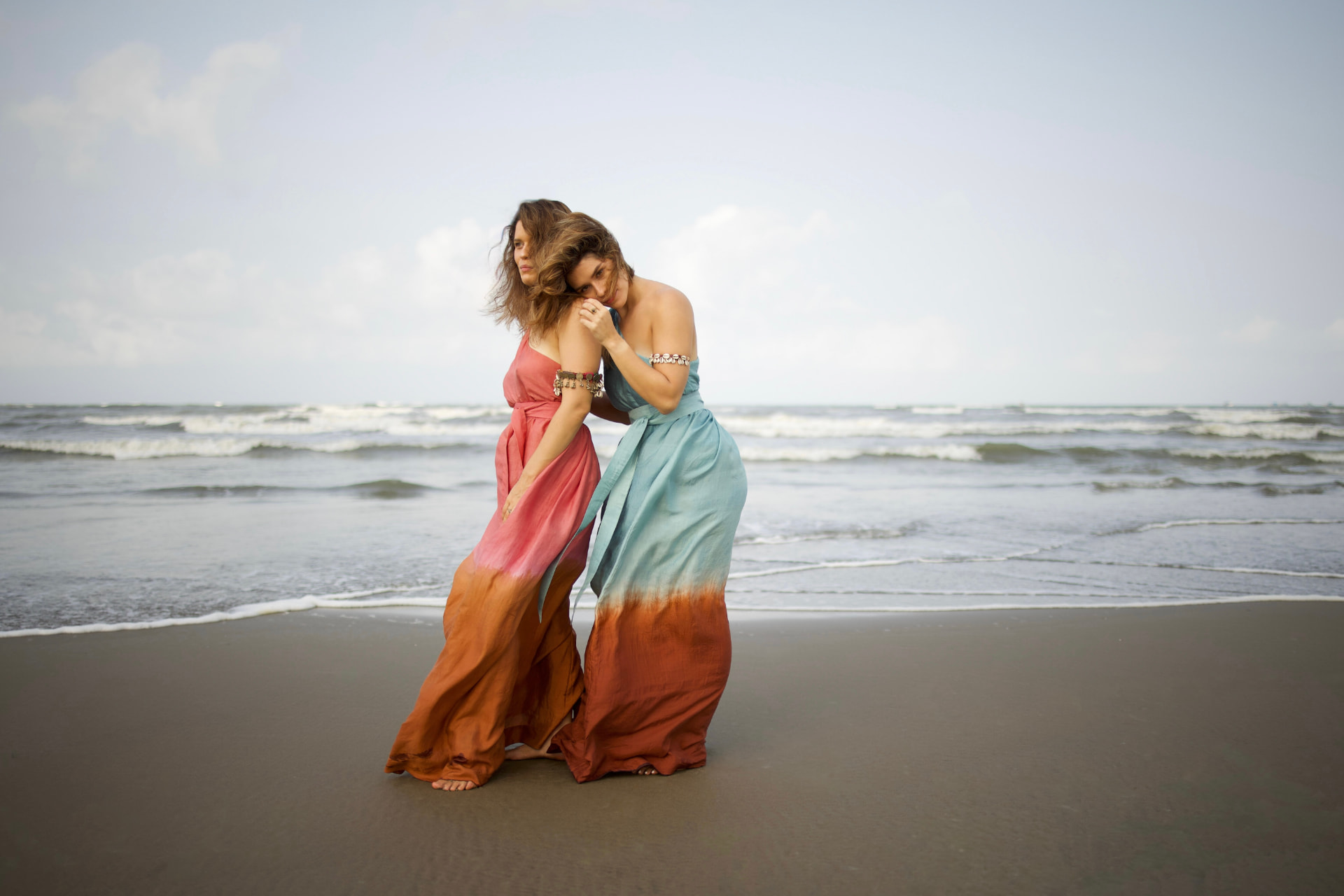 Two women in flowing handwoven Theā Ma dresses on a beach